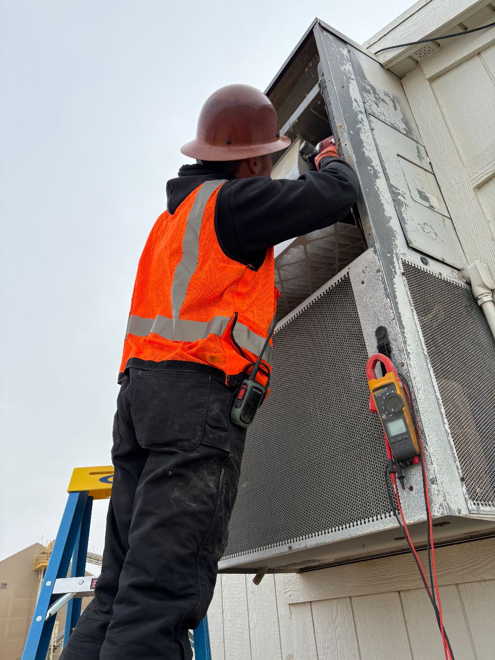 Technician on a ladder metering a large commercial HVAC unit during a service call