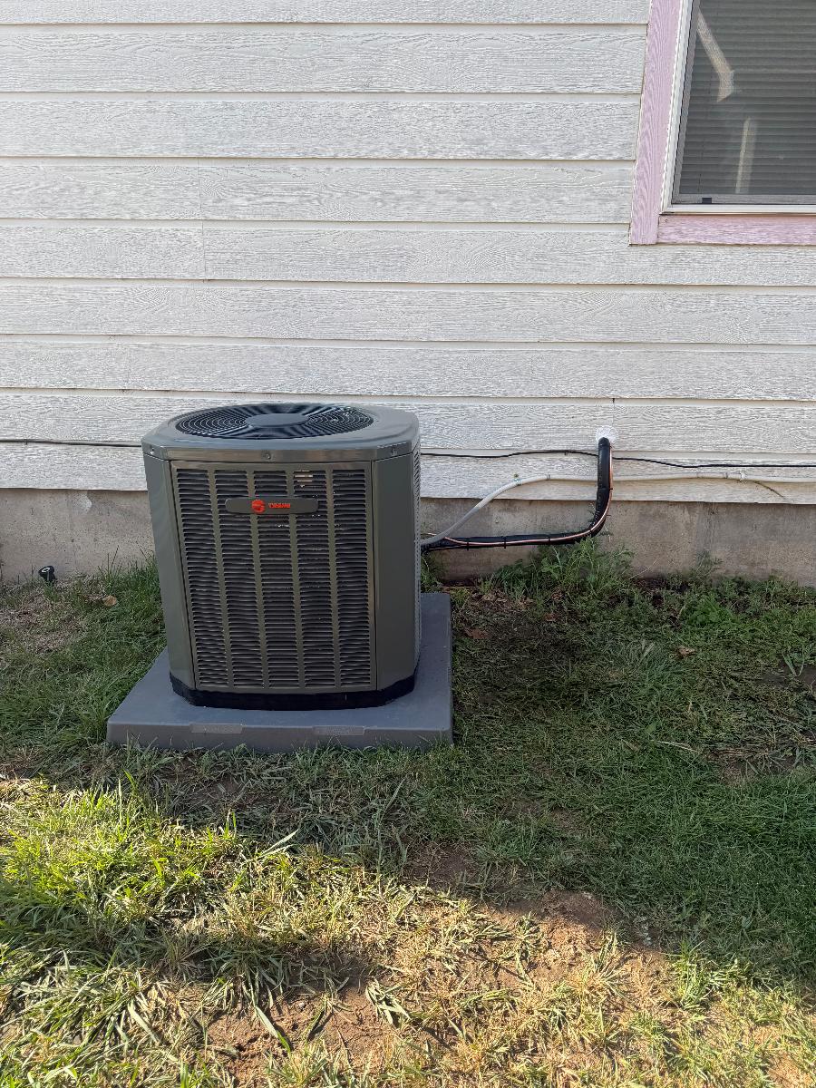 A newly installed outdoor AC condenser set on a pad in a yard